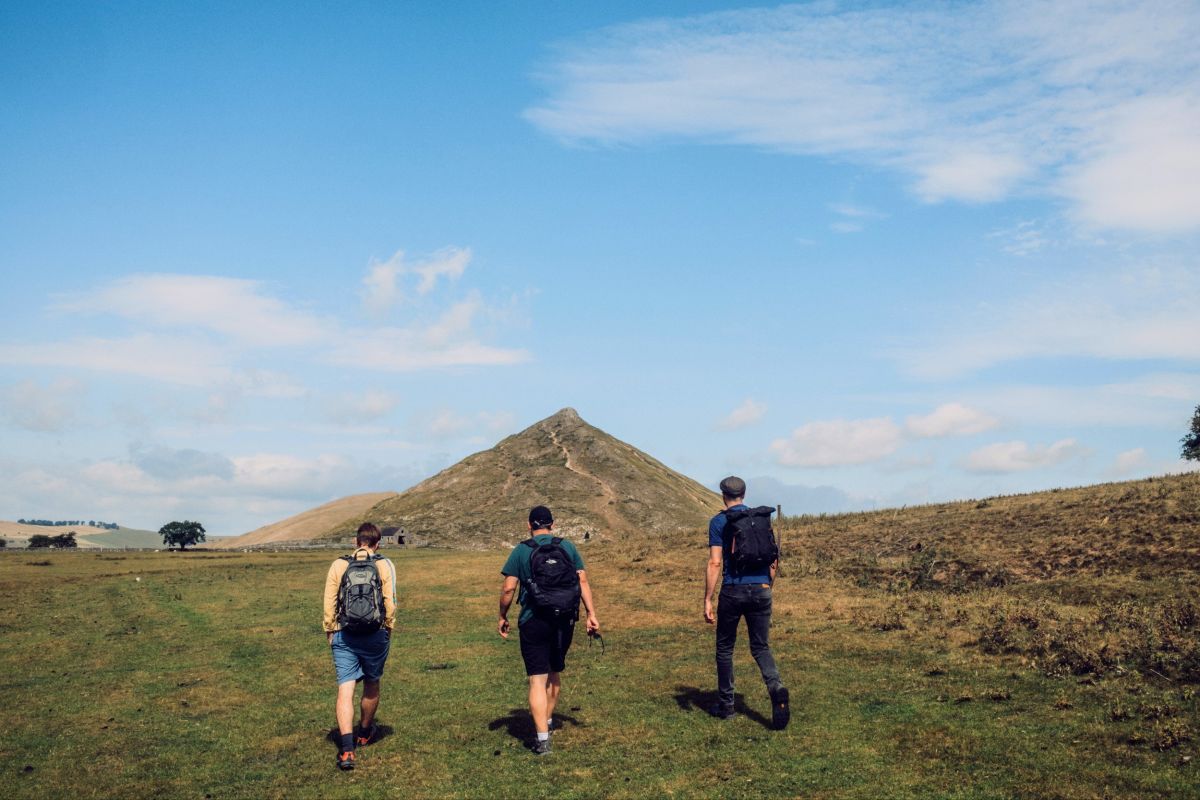 Three men walking under a blue sky towards a conical shaped hill.