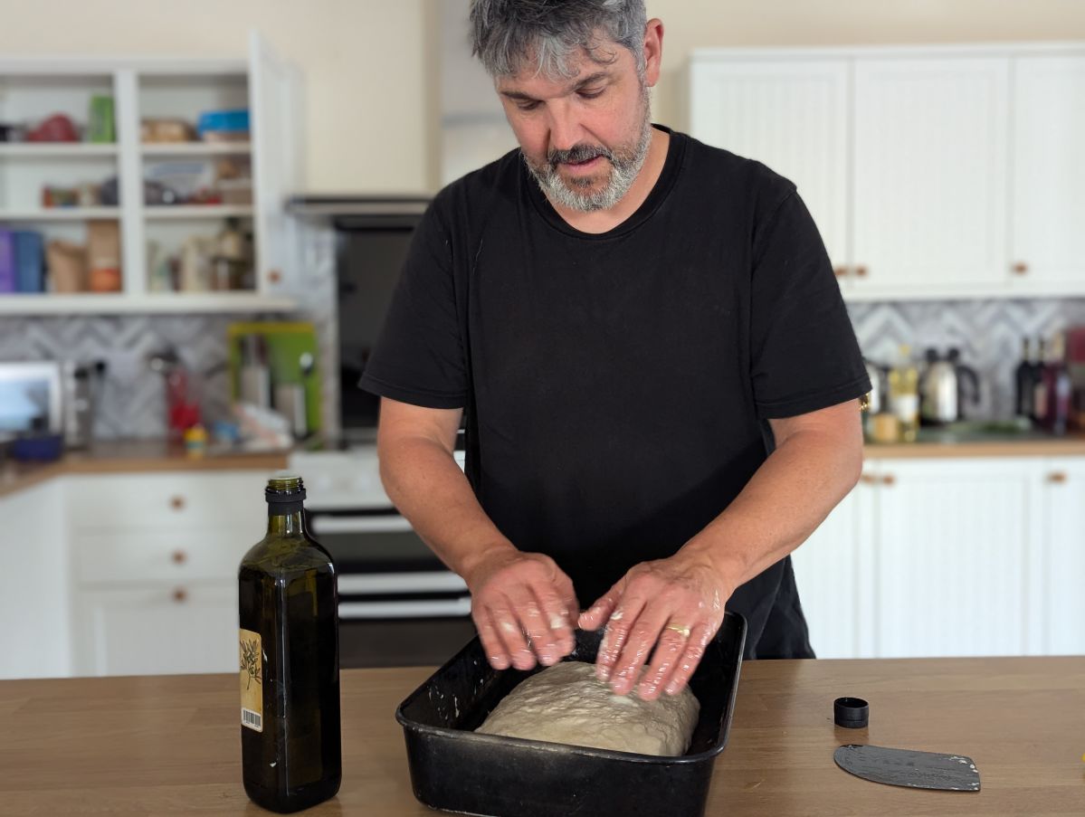 Man in a kitchen making a focaccia in a oven tin.