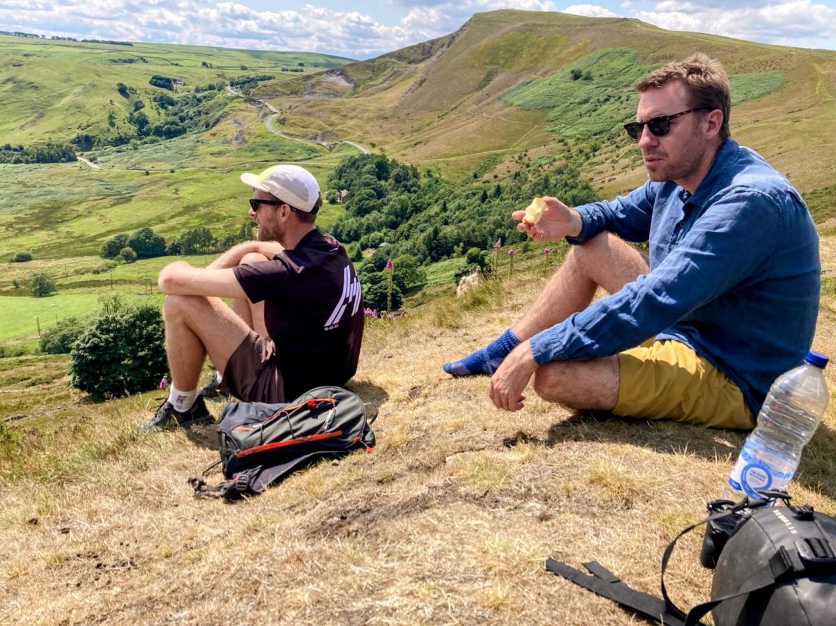 Two men sitting and eating on a ridge with a view.